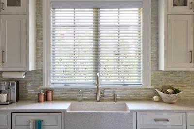 A contemporary kitchen features large window with white faux wood shades.