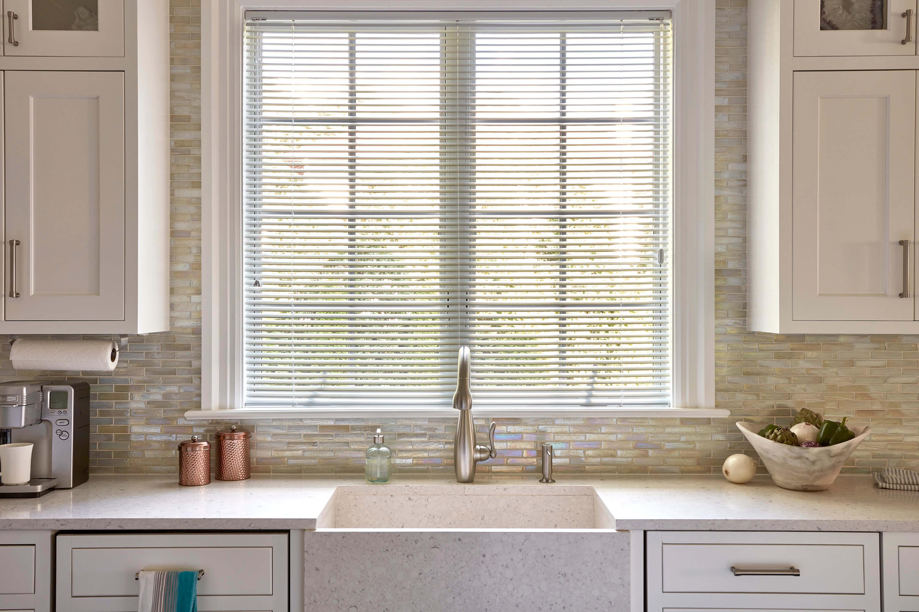 White aluminum blinds cover a large window over a sink.