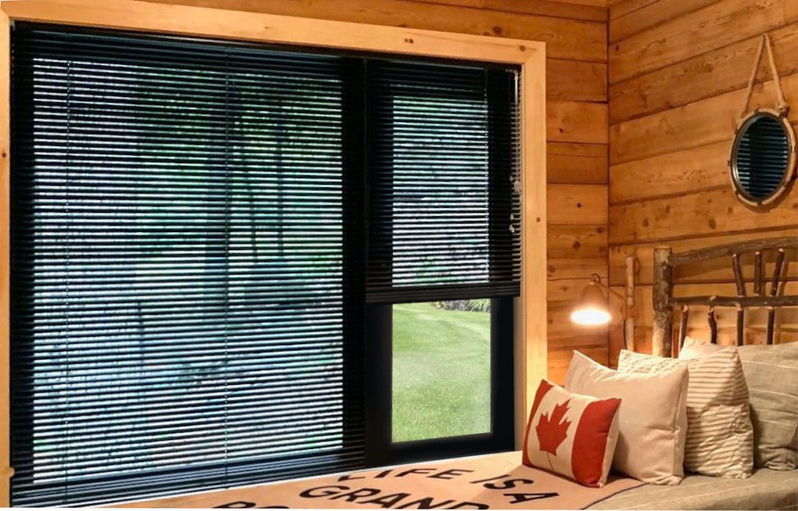 Two matte black mini blinds share one headrail for two side-by-side windows in a modern rustic cabin.