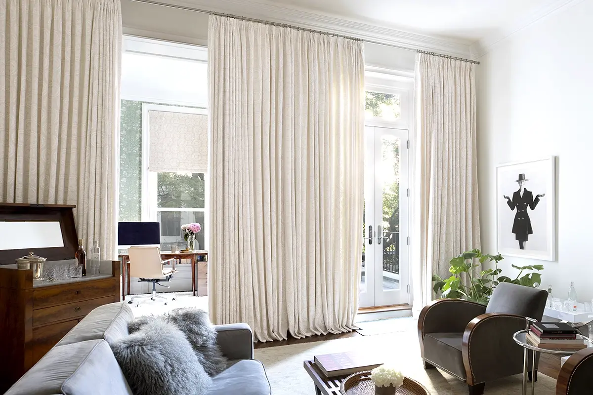 A living room with a large glass doors covered with wall to ceiling ivory colored drapes.
