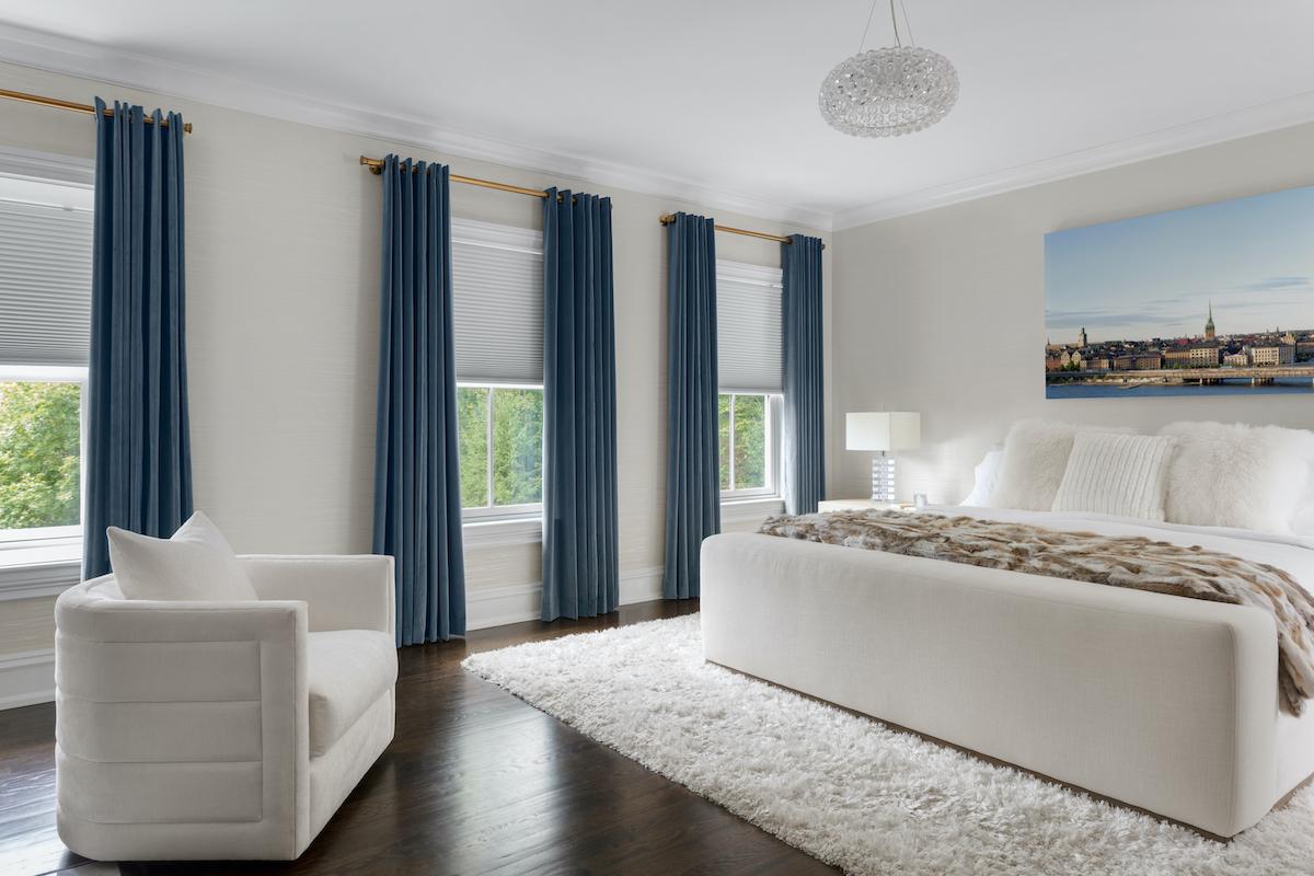A modern bedroom with rich blue velvet custom curtains complementing blackout cellular shades on same windows