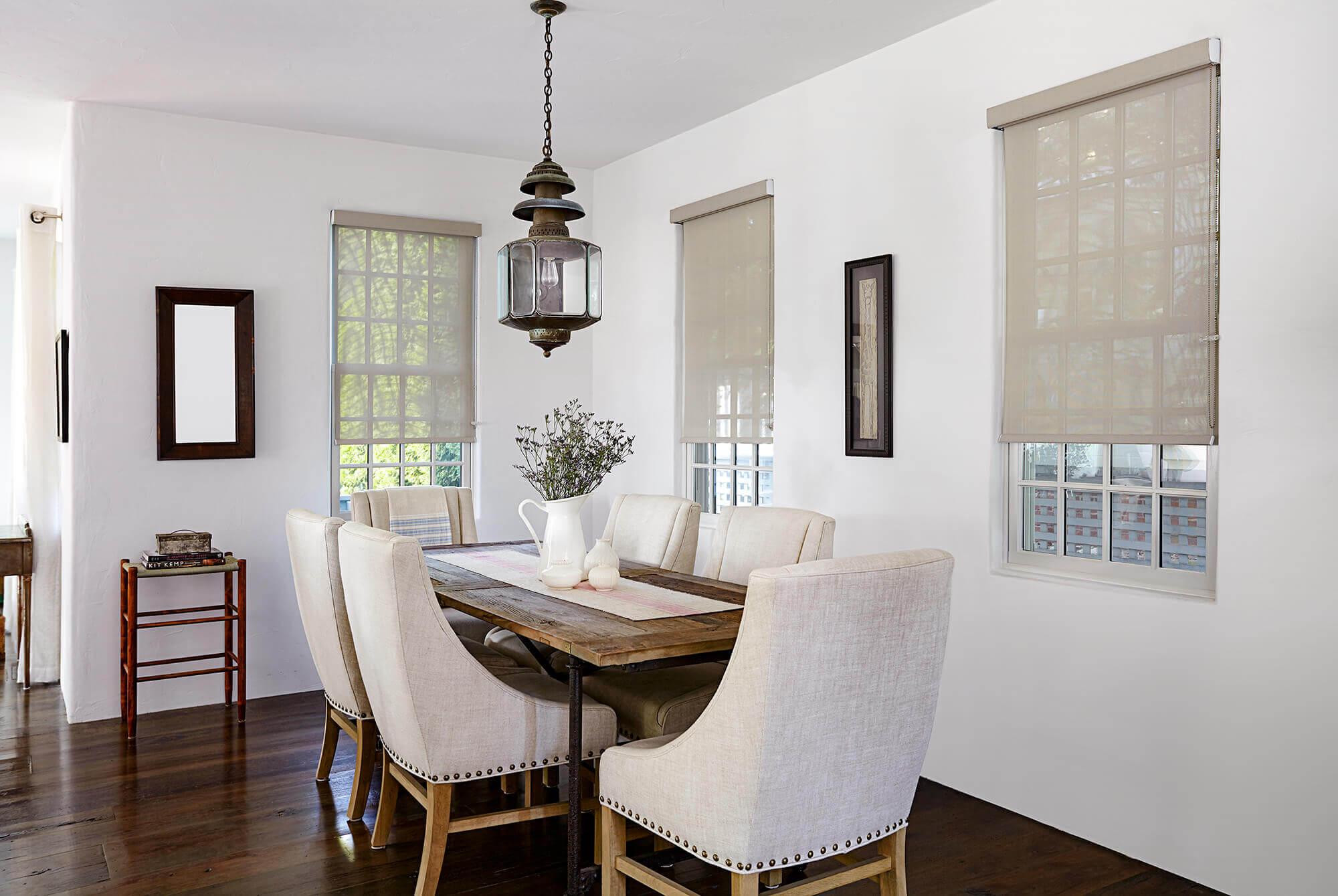 The modern dining room with a lantern looks more cultured with the addition of motorized beige sun shades.