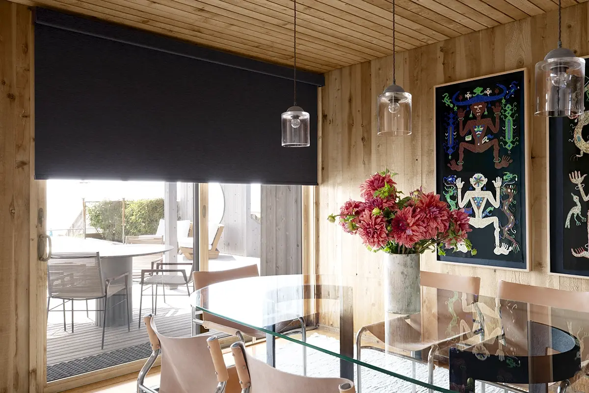 A large black roller shade covers a large sliding glass doors in a modern dining room.