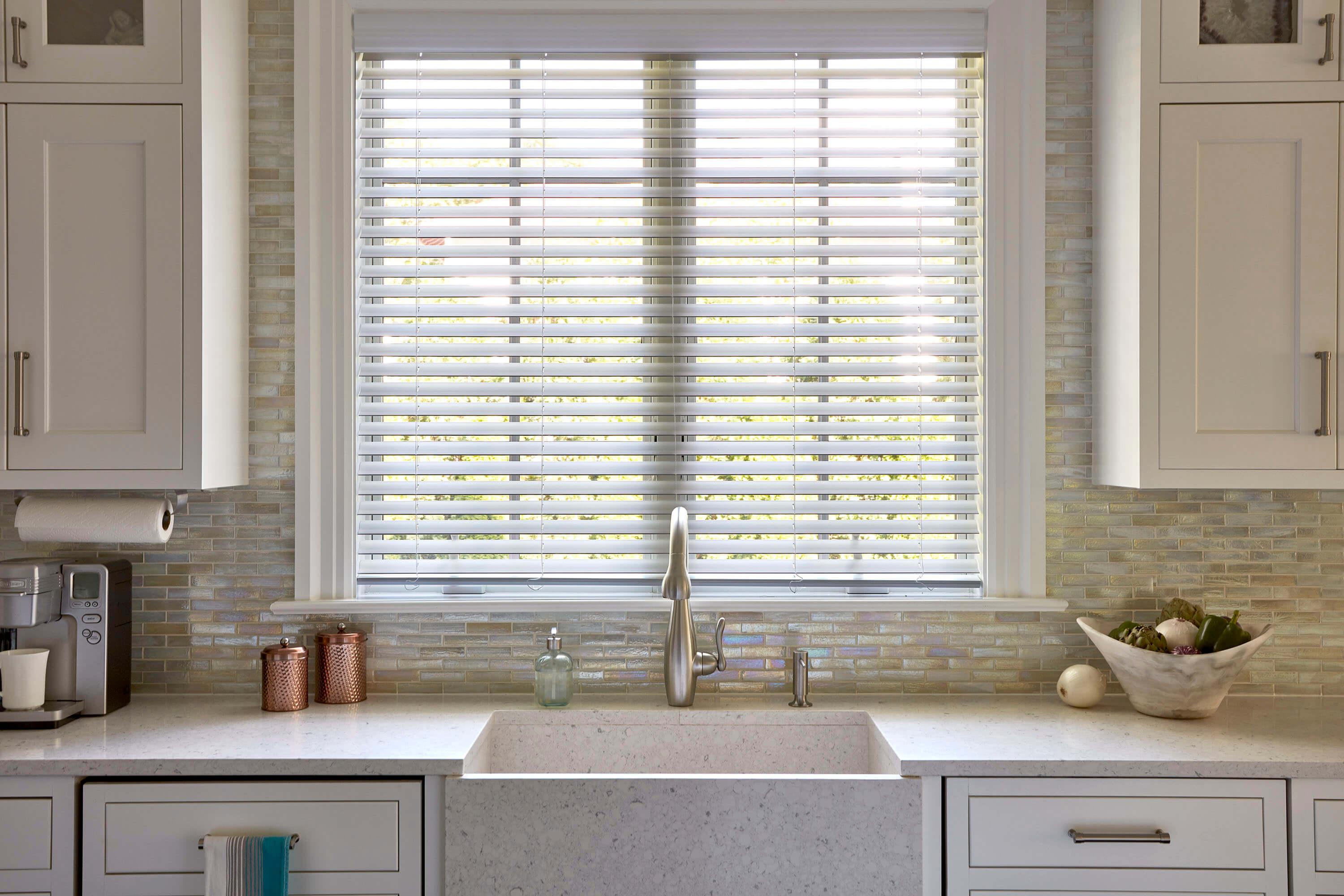 A modern kitchen with stylish white faux wood window blinds on the window above the sink