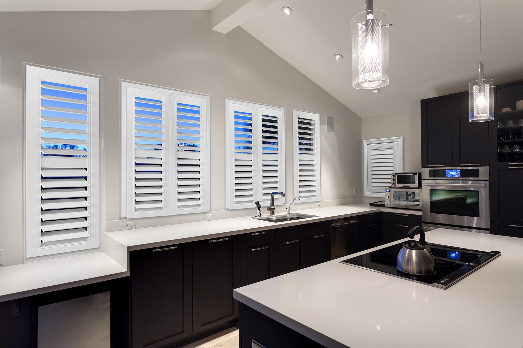 White indoor shutters highlight the airy elegance and appeal of a modern black and white kitchen.