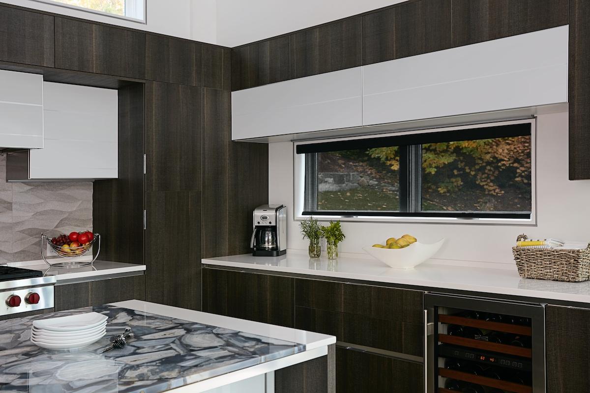 A black solar shade in a modern white kitchen, in the down position, allows full view of the outdoors since it has a very open weave