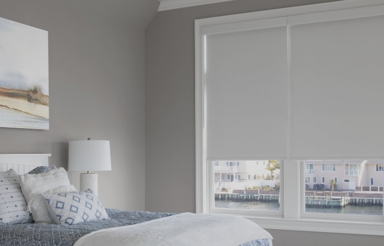 A spacious bedroom has three large windows covered with roller shades.