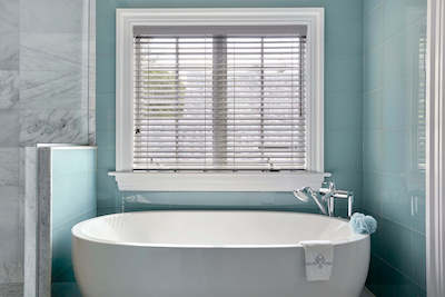 White and blue bathroom with a large tub and light grey faux wood blinds.
