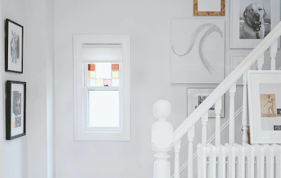 White cellular shades cover a small window at the bottom of the stairs near the front door of a house.