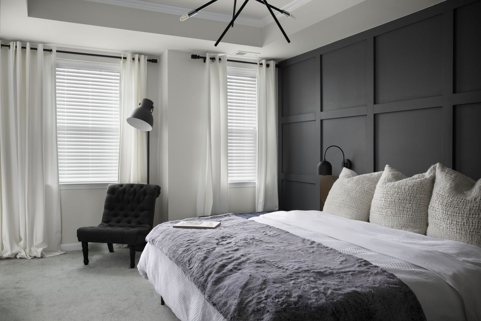 A modern bedroom features white drapery puddling on the flood and paired with white wood blinds.