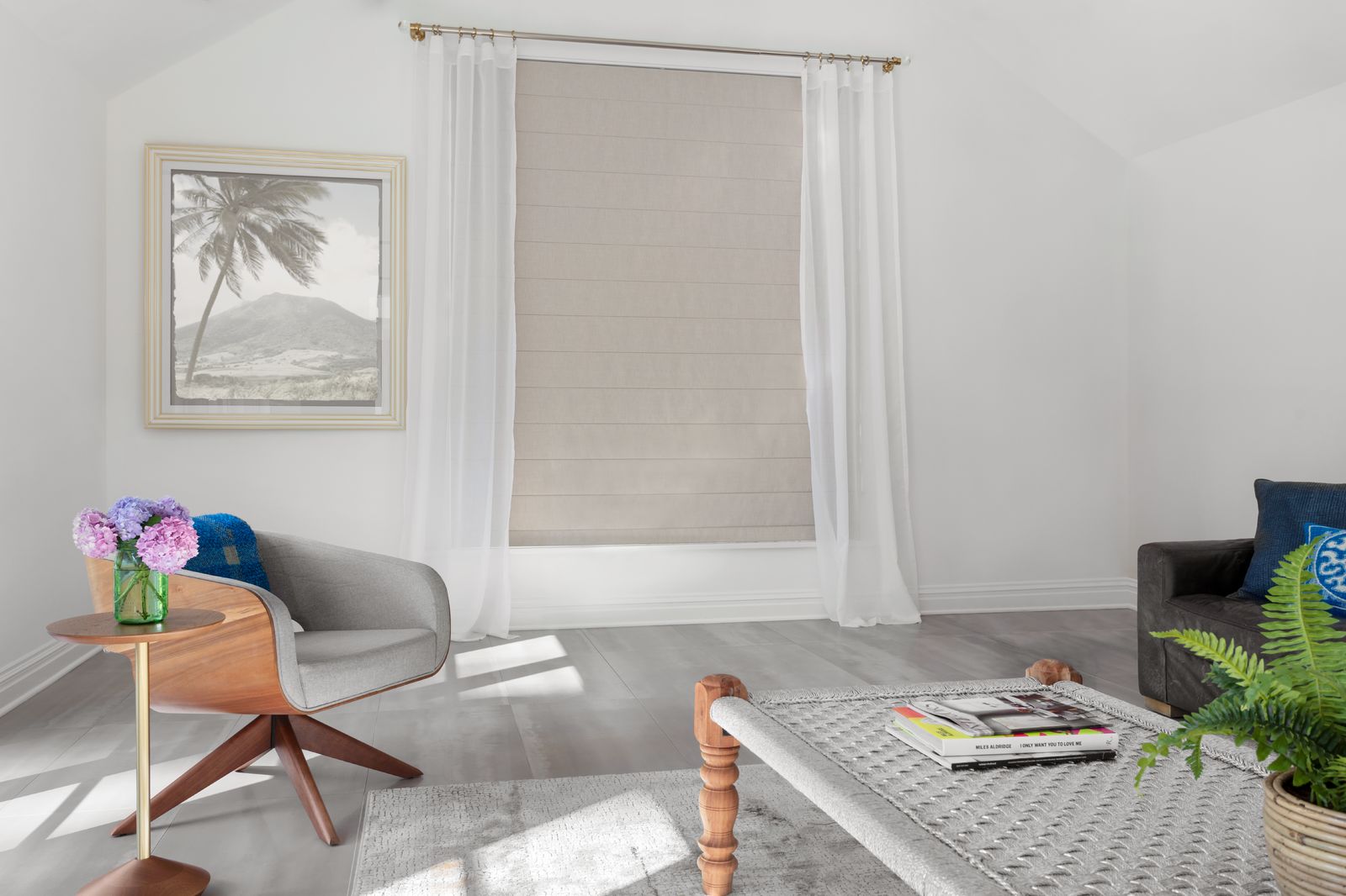 A tan roman shade is paired with sheer drapes in a living room with a modern beach vibe.