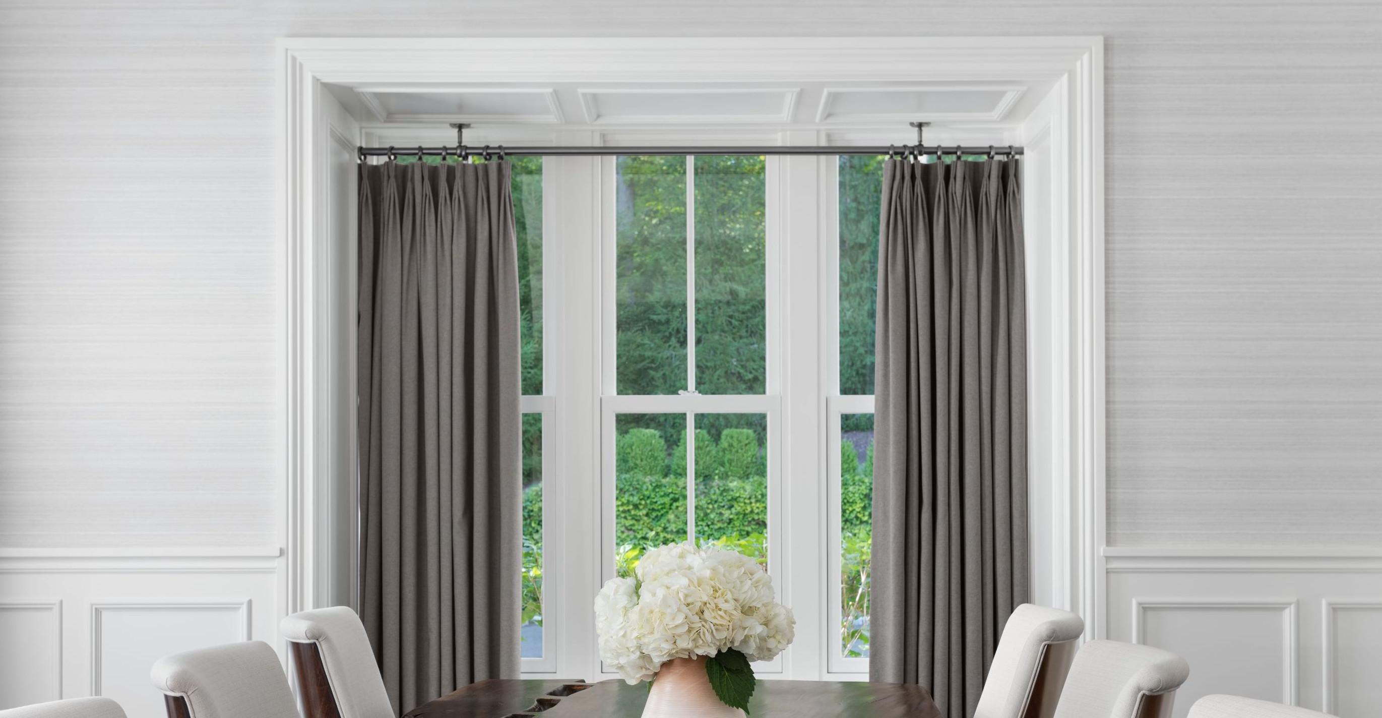 Drapes are hung from ceiling brackets in a window nook containing three side-by-side tall skinny windows.