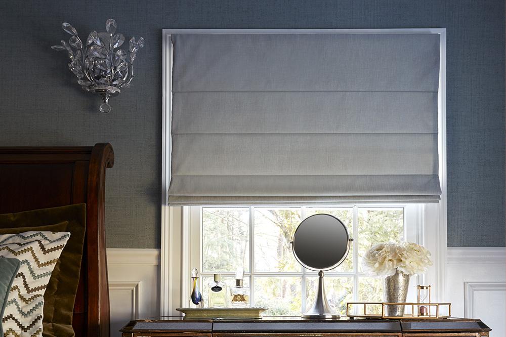 A bedroom has a bedside window covered with a flat Roman shade