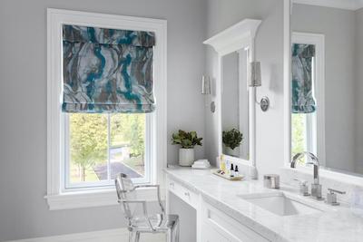 A roman shade with a blue and silver marbled print dresses up a bathroom.