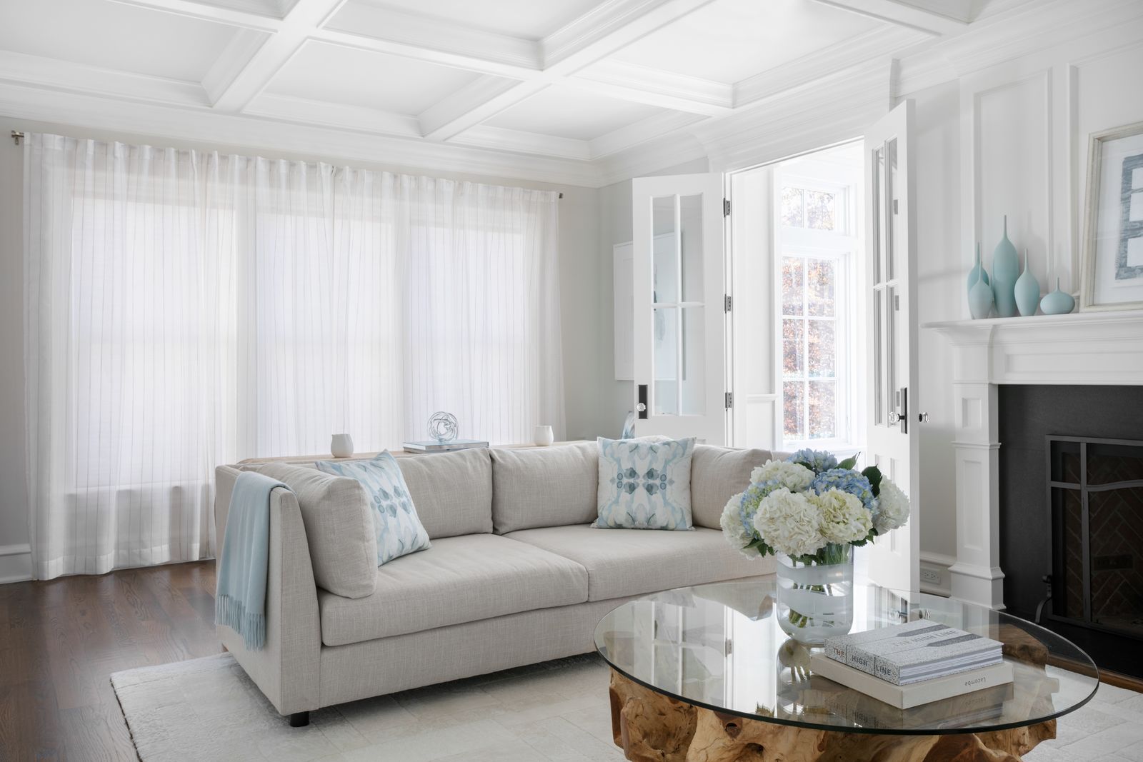 A large window in a modern living room is covered with closed sheer, white drapes 