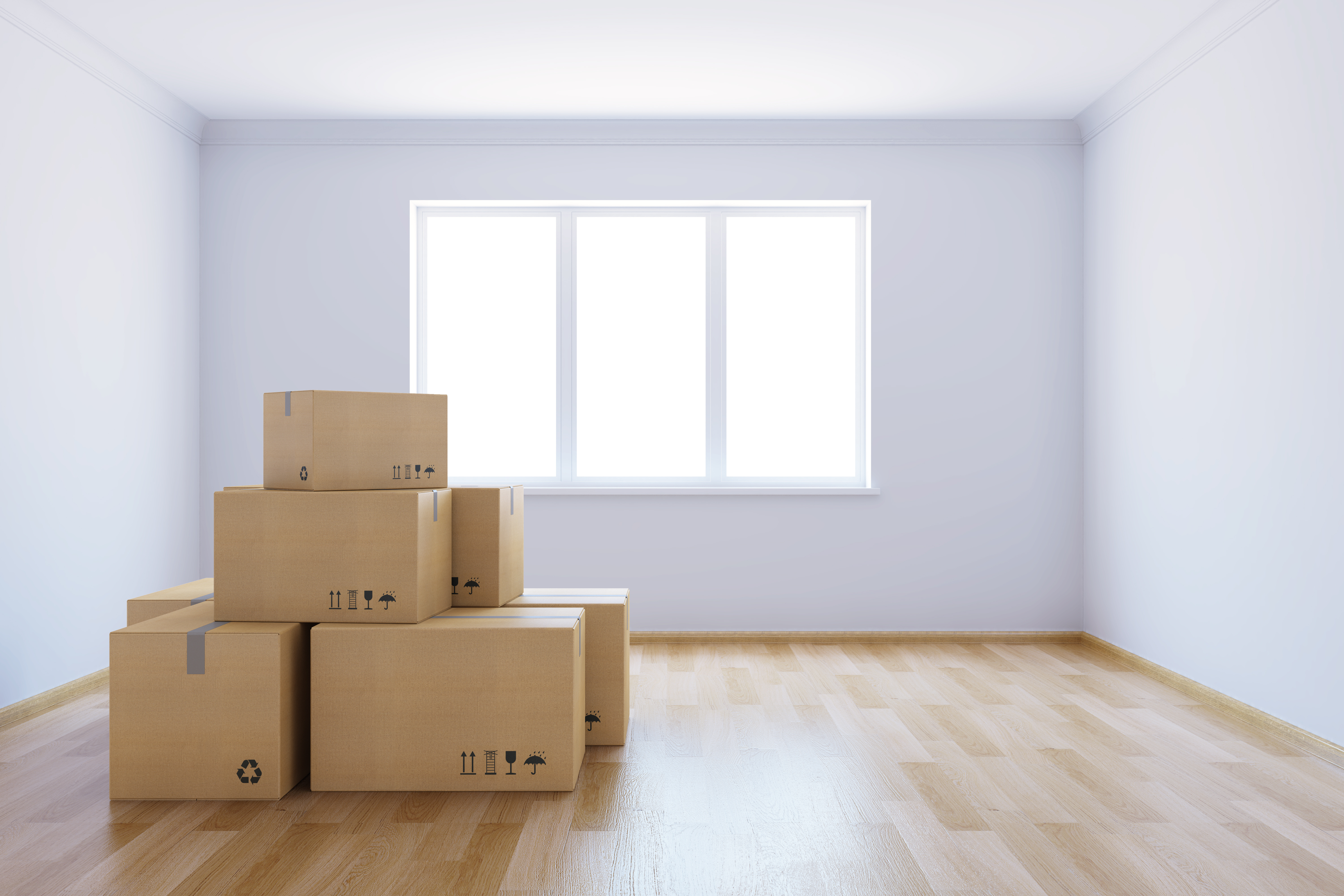 A living room with a giant window is void of items all except a pile of moving boxes.