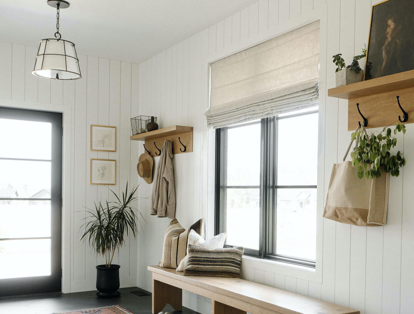Roman shades cover a large window in a modern farmhouse-styled mudroom.