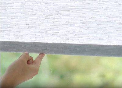A close-up image of a single finger lifting a cordless roller shade up from the bottom bar.
