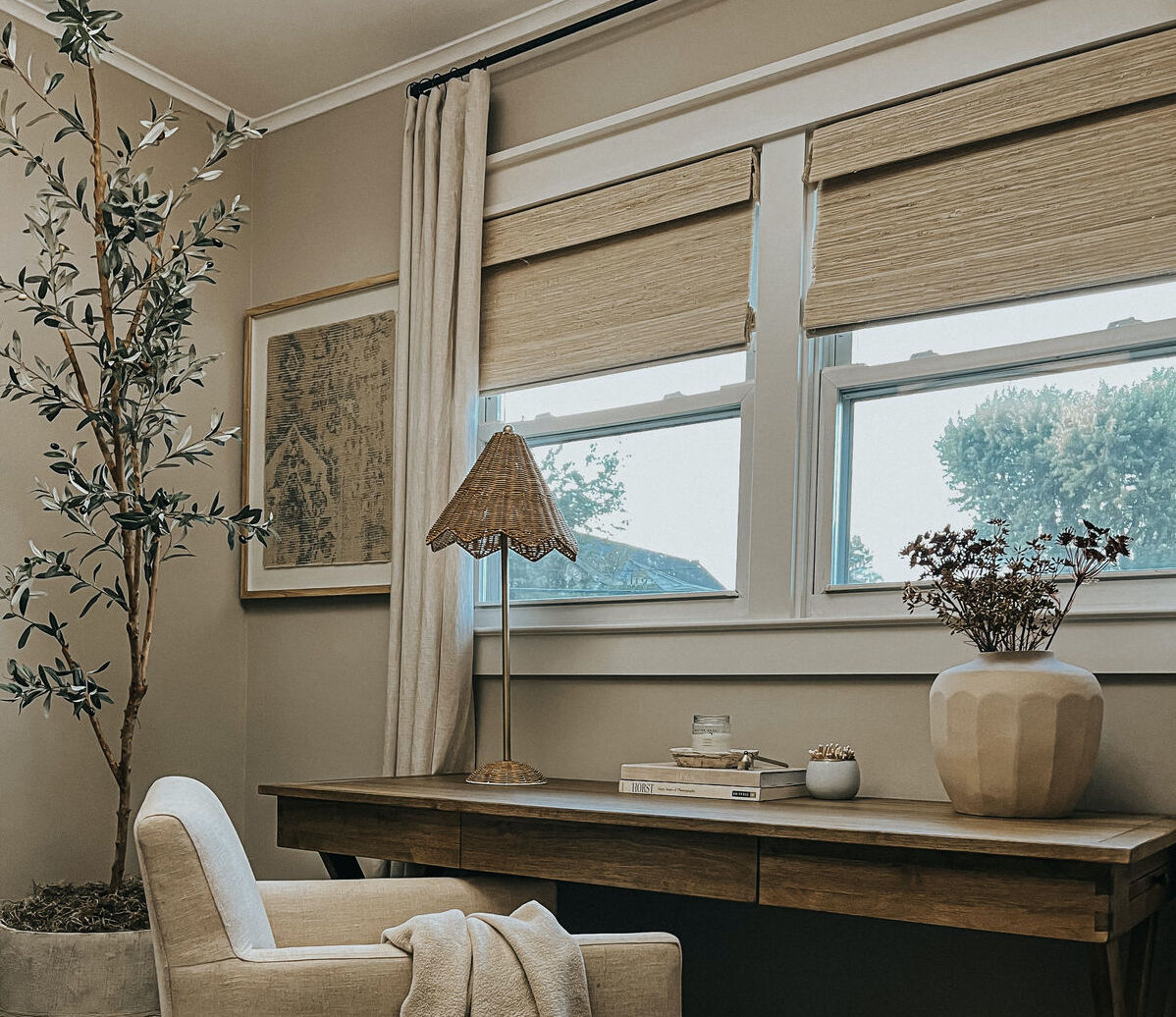 A window in a modern home office space features woven wood shades paired with drapes 