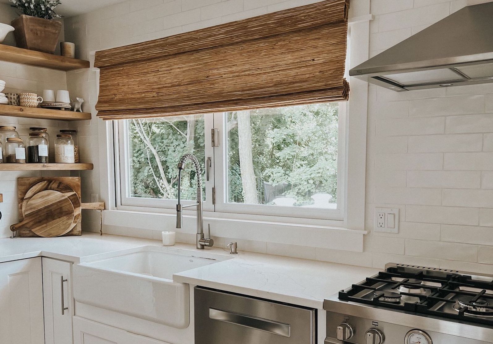 Rustic woven wood shades cover a large window above a large farmhouse-style sink in a modern kitchen.