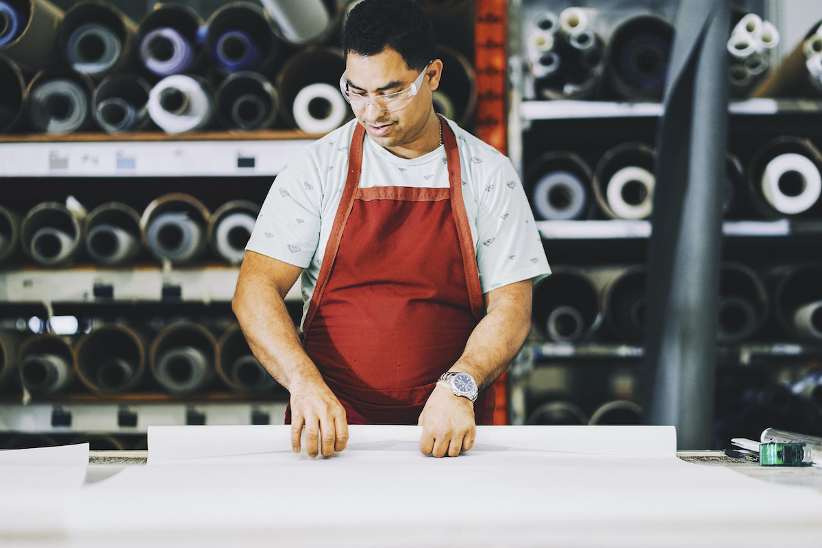 A factory worker in an apron rolls out a pattern on a large table.