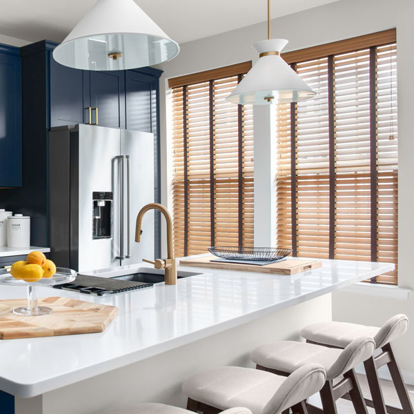 De superbes stores en bois véritable dans des tons naturels recouvrent un mur de fenêtres dans une cuisine moderne dotée d'armoires bleu foncé.