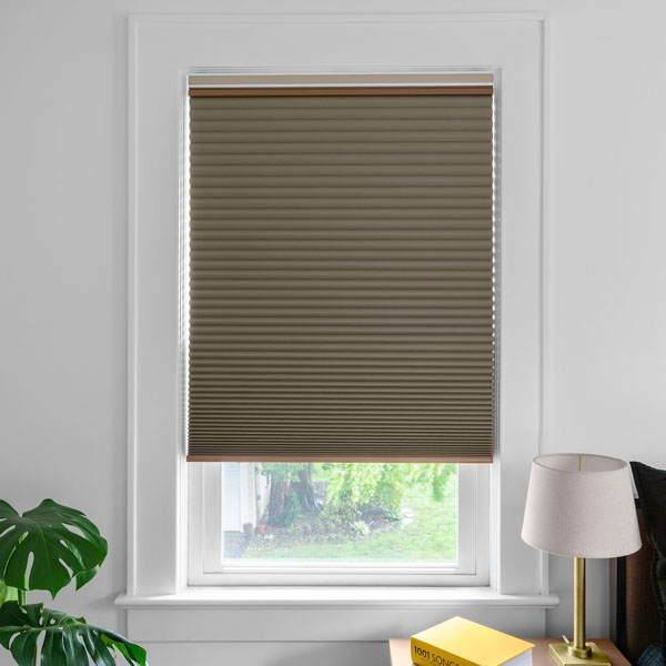 A tan colored, blackout cellular shade left slightly open allows light to pour into a room.