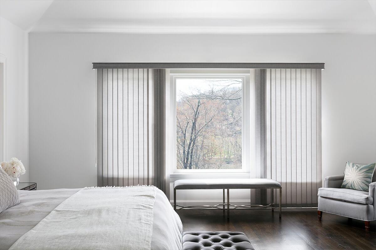 Grande chambre à coucher décorée avec des stores verticaux faits avec un tissu gris clair