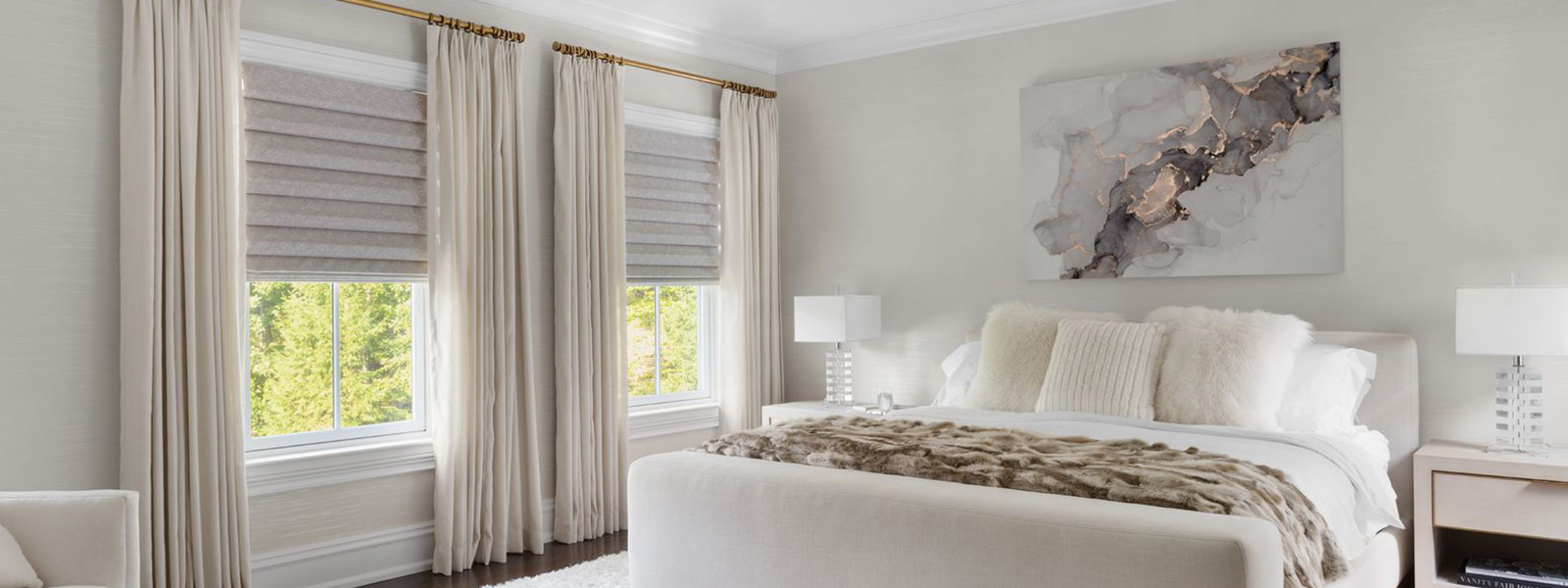 Drapes paired with roman shades on a double window in a modern bedroom. Des rideaux agencés à des stores romains décorent une double fenêtre dans une