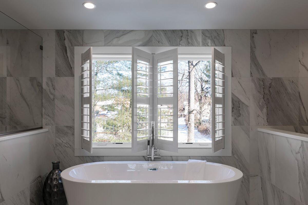 Salle de bain en blanc et gris marbre avec une grande baignoire et des persiennes blanches