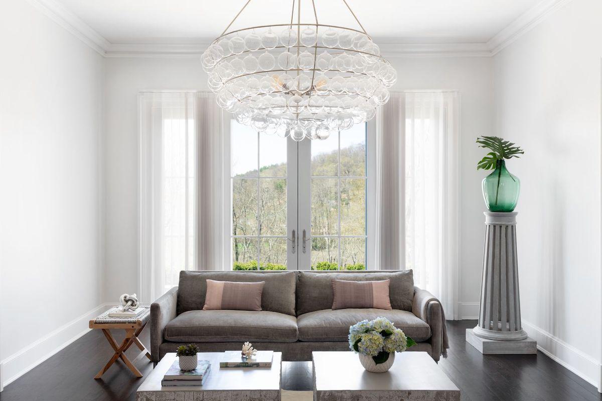 An elegant living room features a modern chandelier and tall windows and french doors partially covered by Melody sheer shades