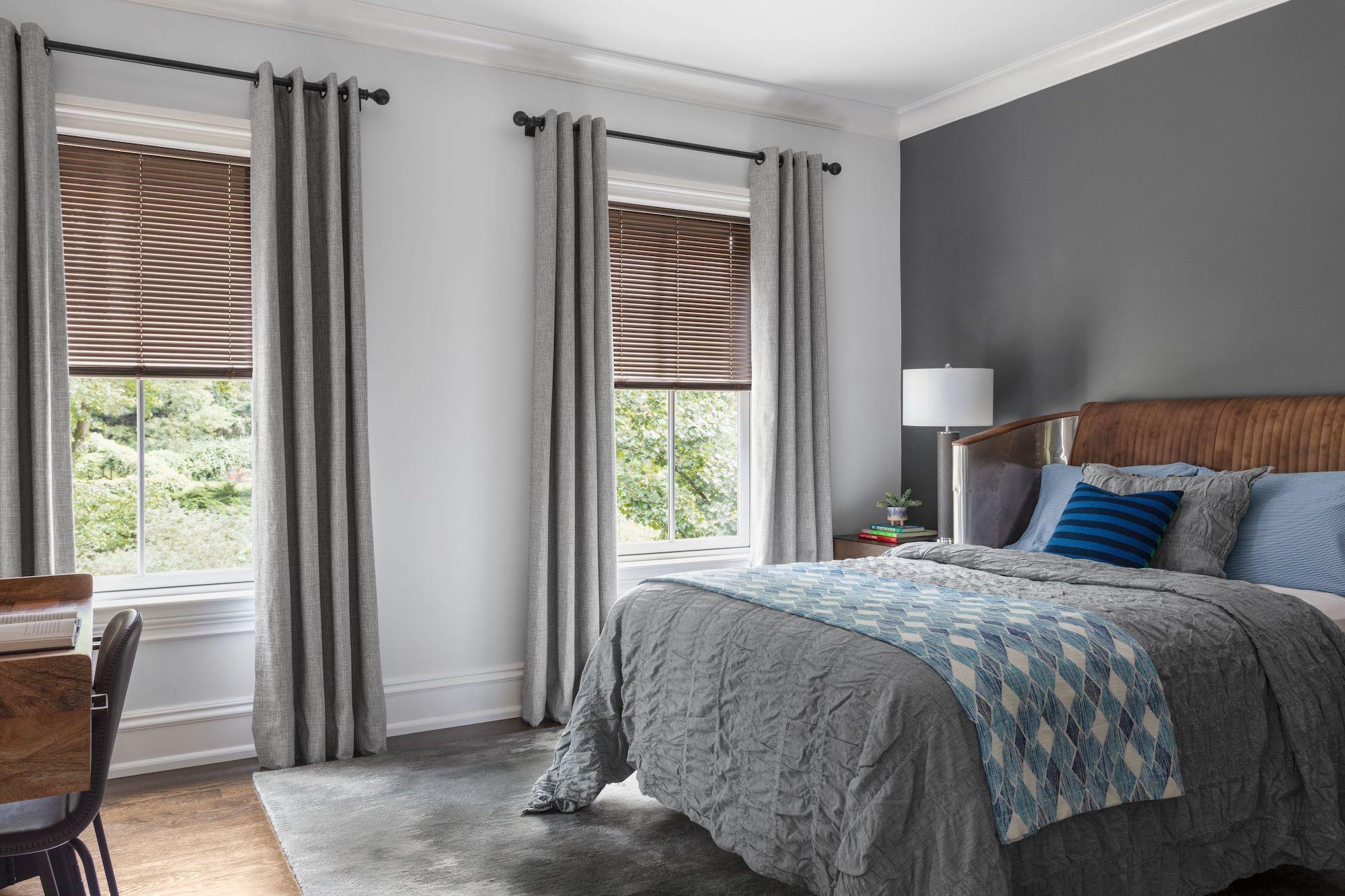 Aluminum blinds are paired with curtains on two windows in a modern bedroom
