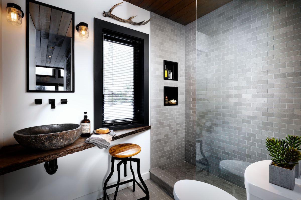 A small modern, rustic bathroom features a window with a black window frame & matte black mini blinds
