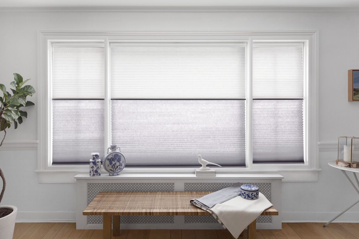 Day and night cellular shades cover three large windows in a bright dining room.