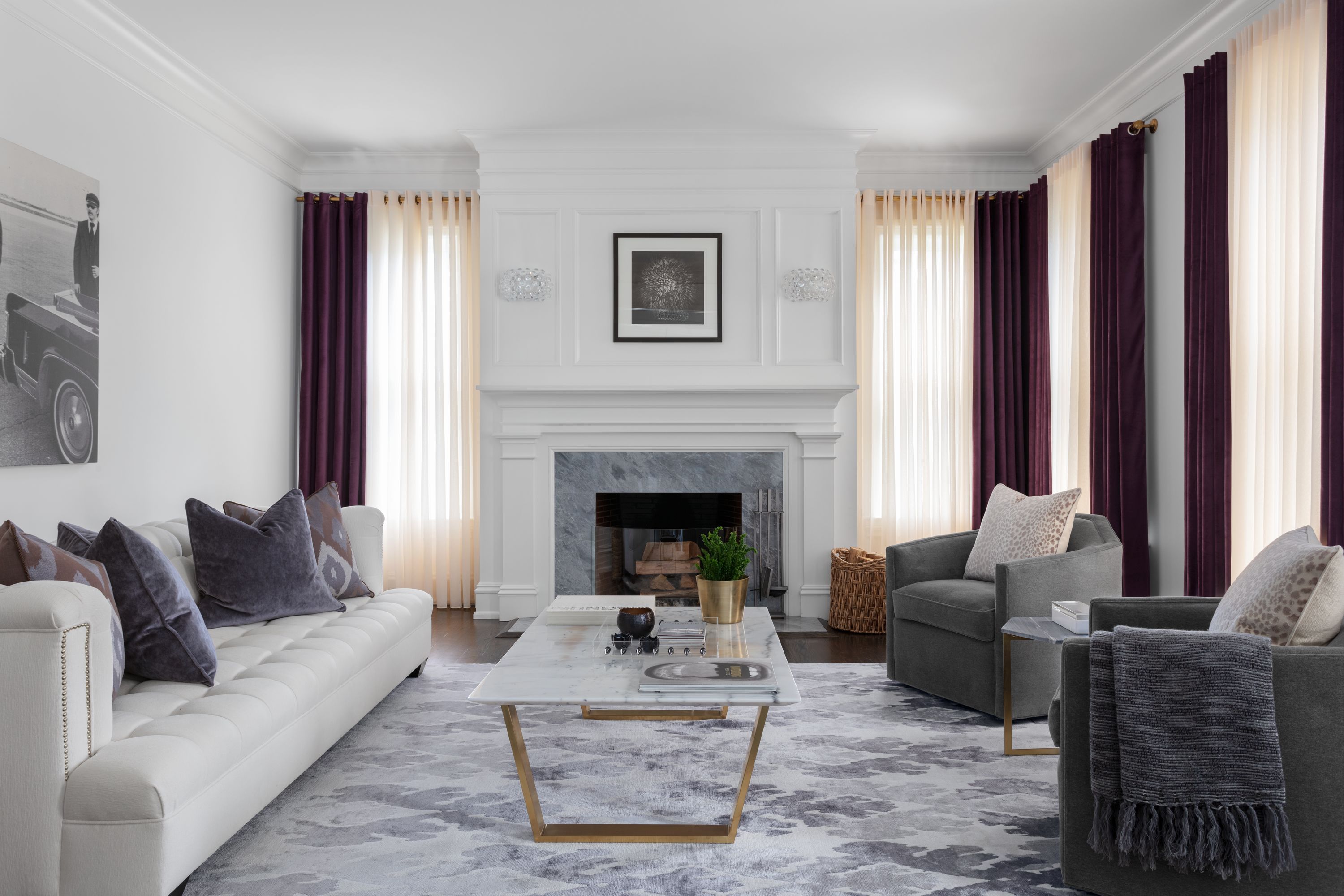A modern living room with large windows features sheer white drapery paired with purple velvet drapes