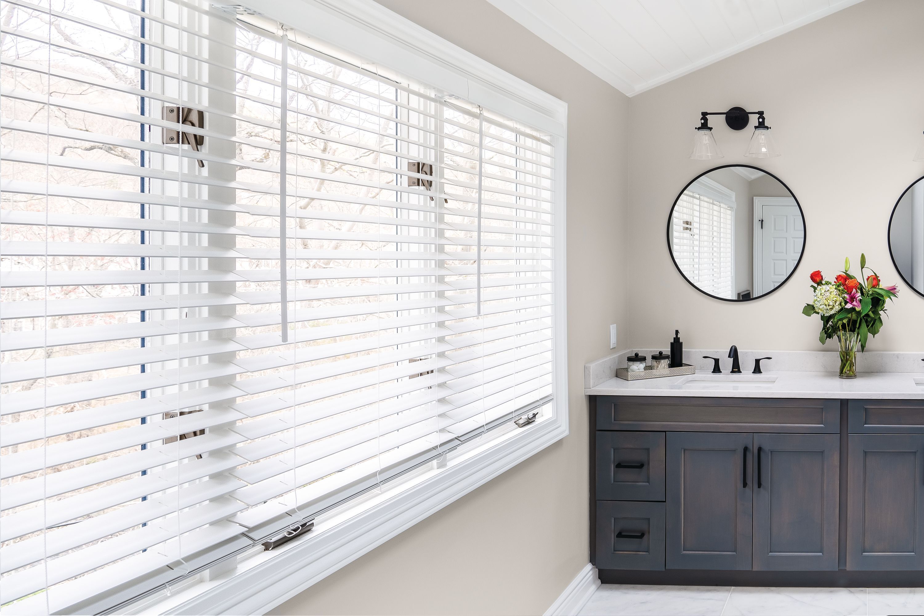 White faux wood blinds cover a large window in a bright bathroom.