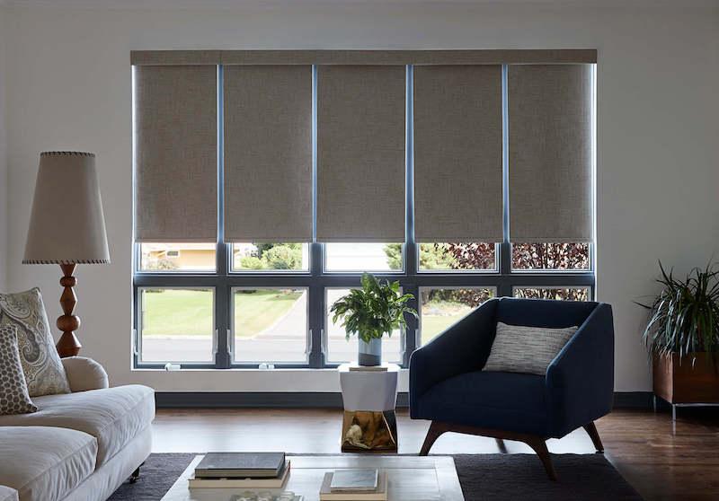 Five adjacent tall windows in a contemporary living room feature individual room-darkening roman shades in a neutral tan color.