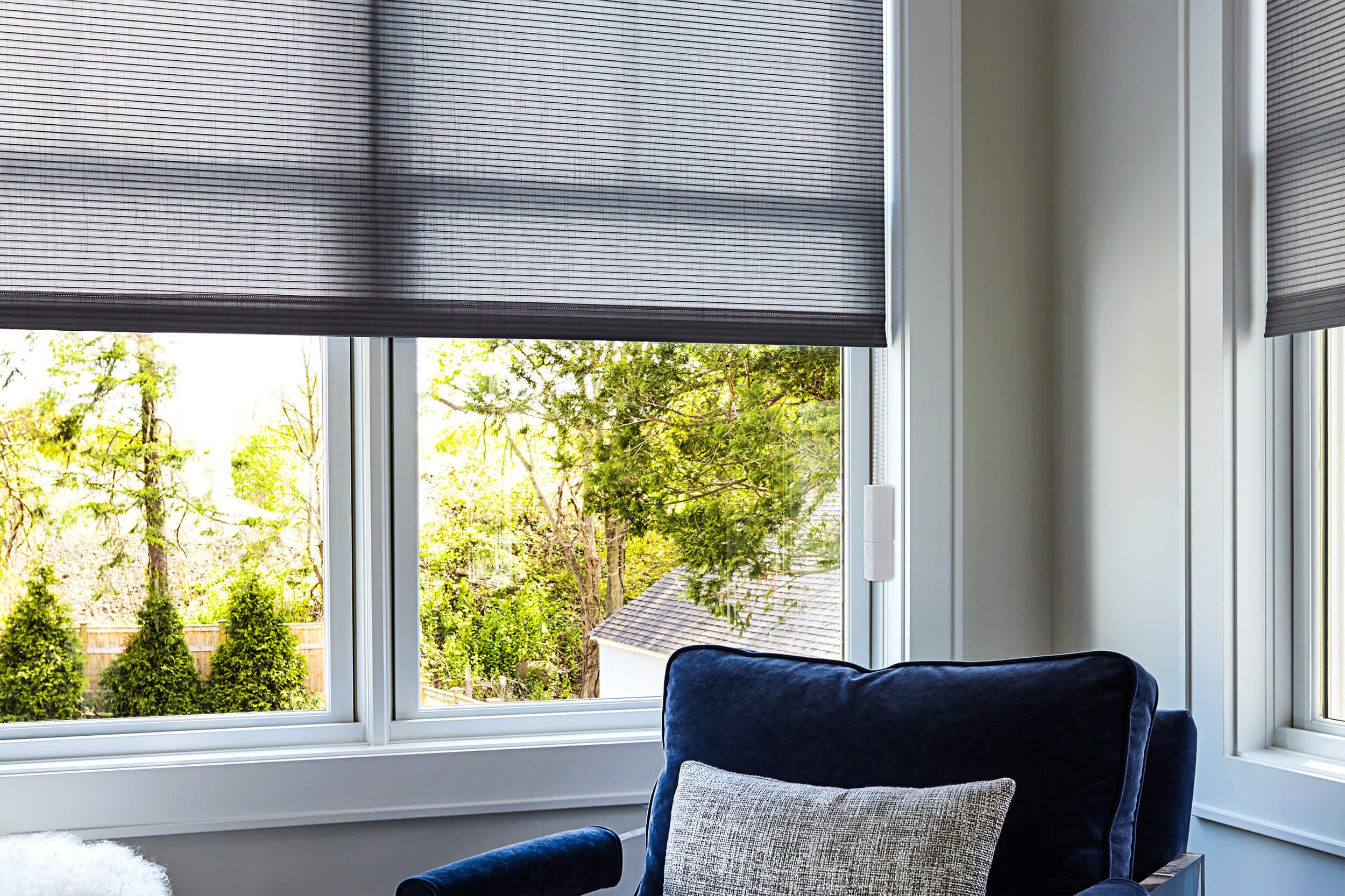 A large window in a contemporary living room features the MOVE unit for retrofitting your existing blinds and shades with motorization capabilities.