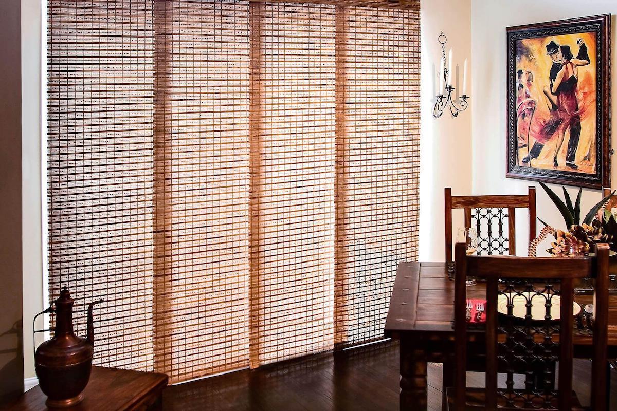 Des stores à panneaux coulissants confectionnés avec un tissu « toile solaire » de ton beige filtrant la lumière offrant de l’intimité à un salon convivial.
