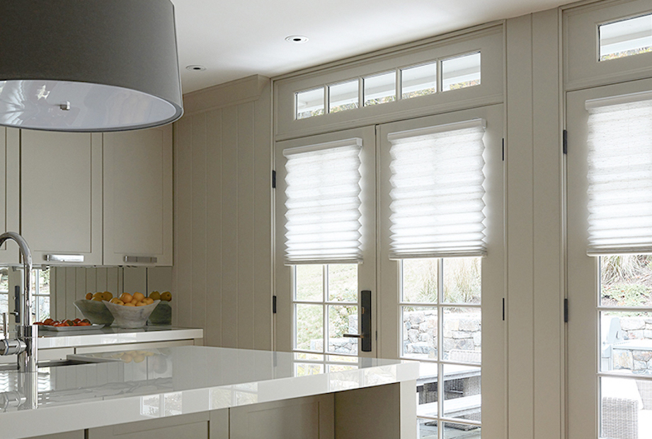 A modern kitchen features white grand pleat pleated shades on french doors.