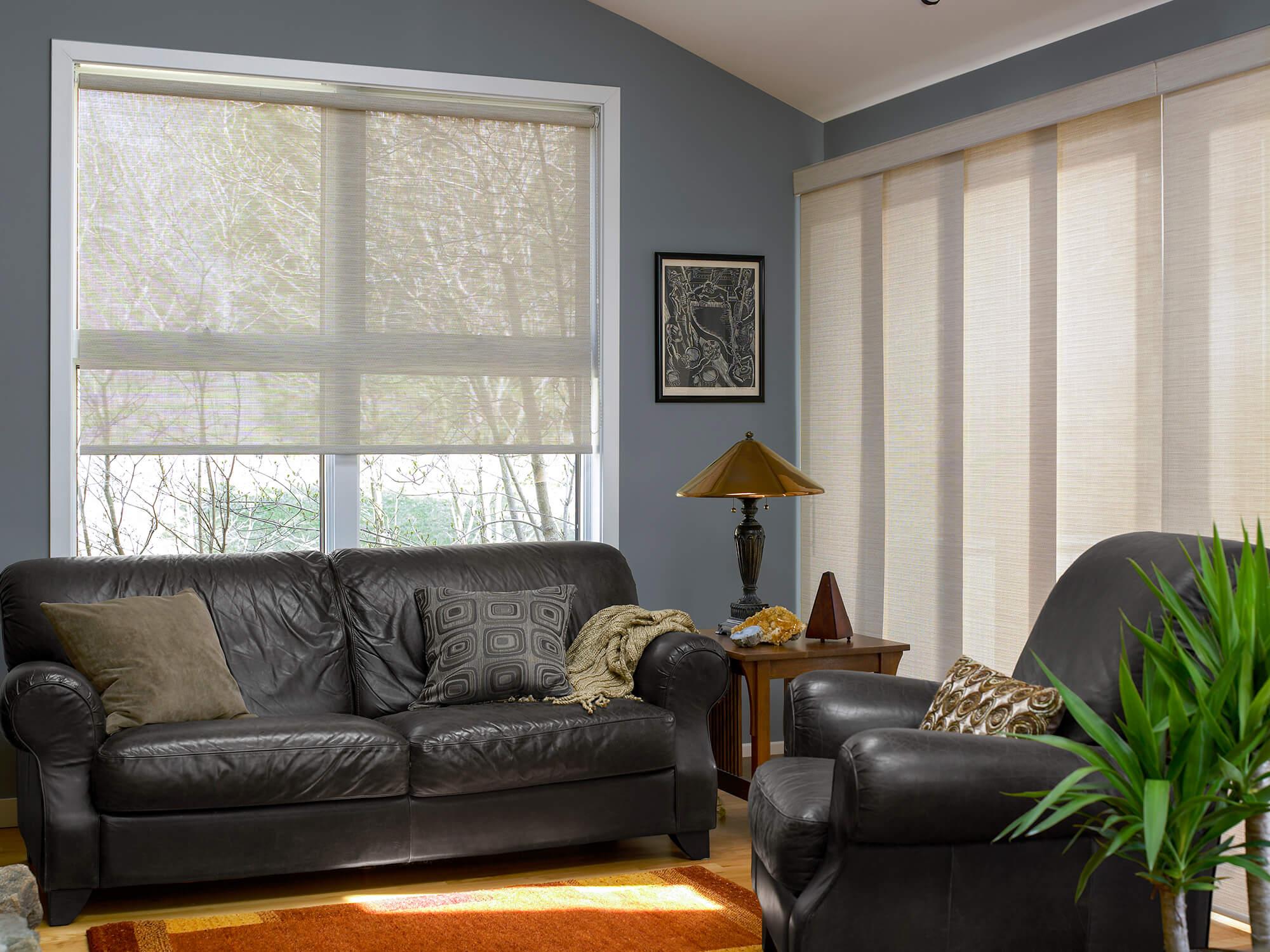 Un salon avec une fenêtre recouverte d’une toile solaire et une porte vitrée avoisinante embellie avec des stores à panneaux coulissants confectionnés avec le même tissu que celui de la toile.