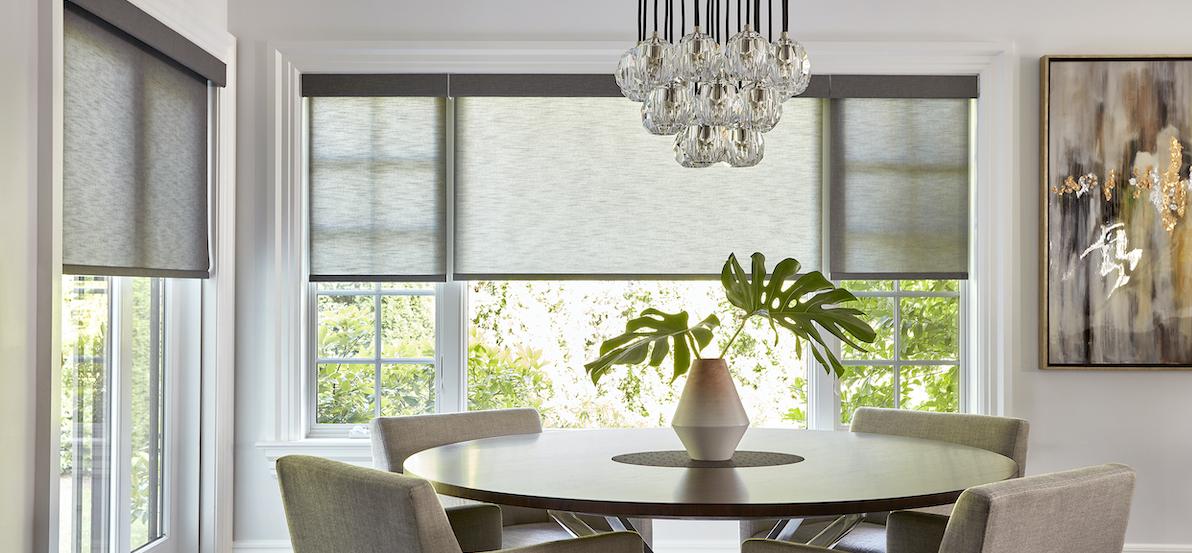 A modern dining room showcases roller shades on large glass doors and a large window.”  alt=