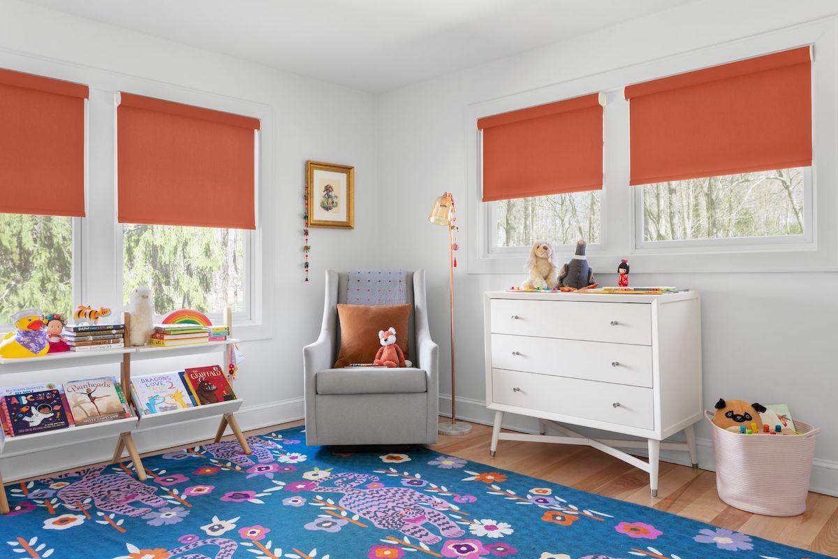 A fun and bright child's play room has four windows with orange roller shades