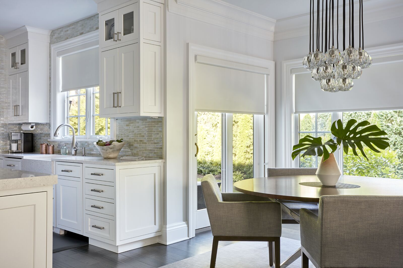A kitchen and adjacent dining nook both feature white roller shades