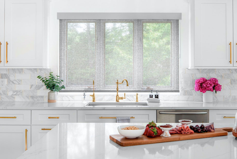 A kitchen has three windows covered with light grey solar shades.