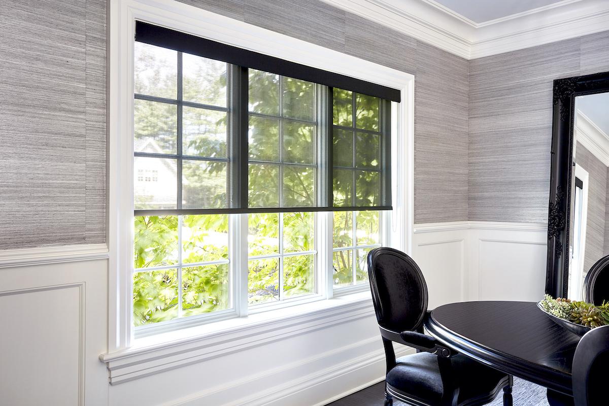 Une salle à dîner blanche et grise avec une toile solaire diaphane de ton noir offrant une vue non obstruée vers l’extérieur.