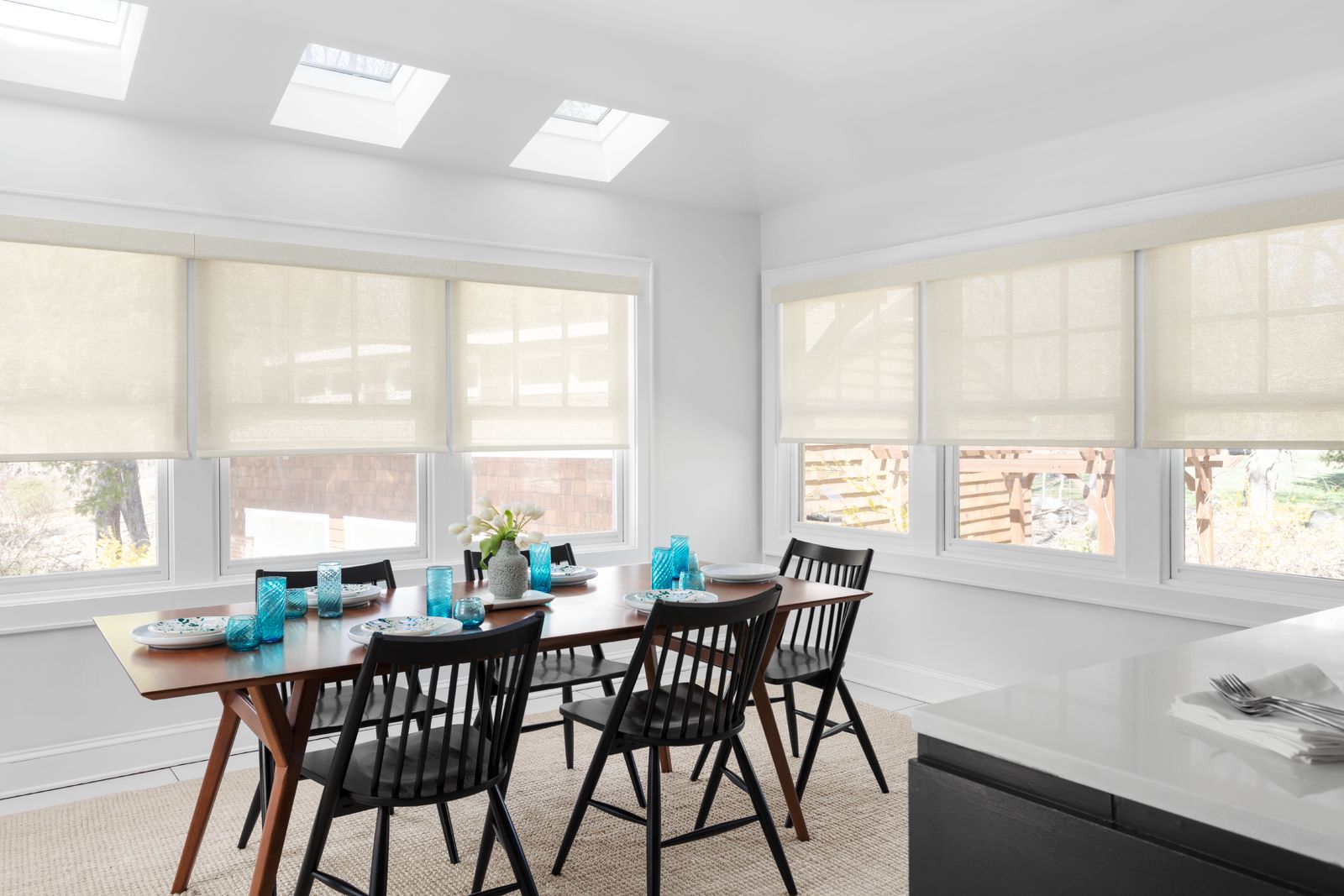A solar shade blocks the harsh sun yet allows light and a view to come through a wall of windows in a modern dining room.