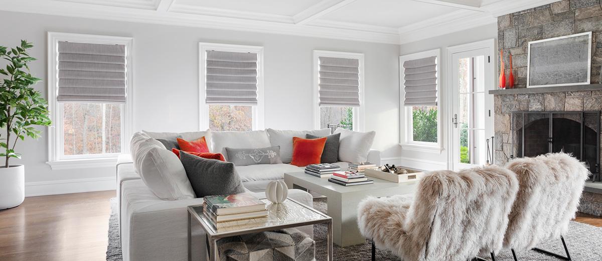Grey cordless roman shades lend a modern look to four windows in a living room.