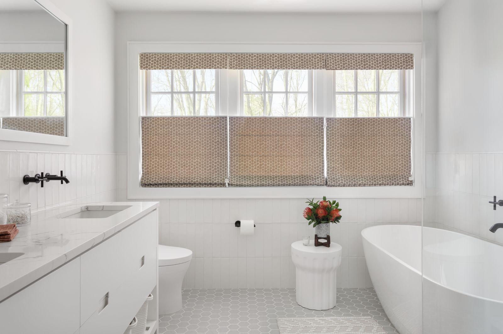 Three side-by-side tan top-down bottom-up roman shades allow light to come in from the top of the shades in a large, modern bathroom