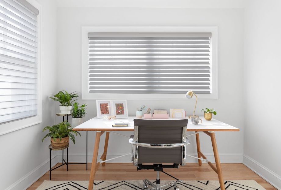 A modern home office features a large window covered with a light grey Serenity sheer shade.